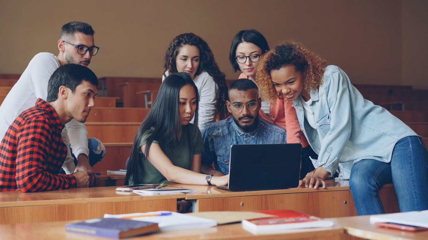 Students collaborating around a laptop in a university classroom