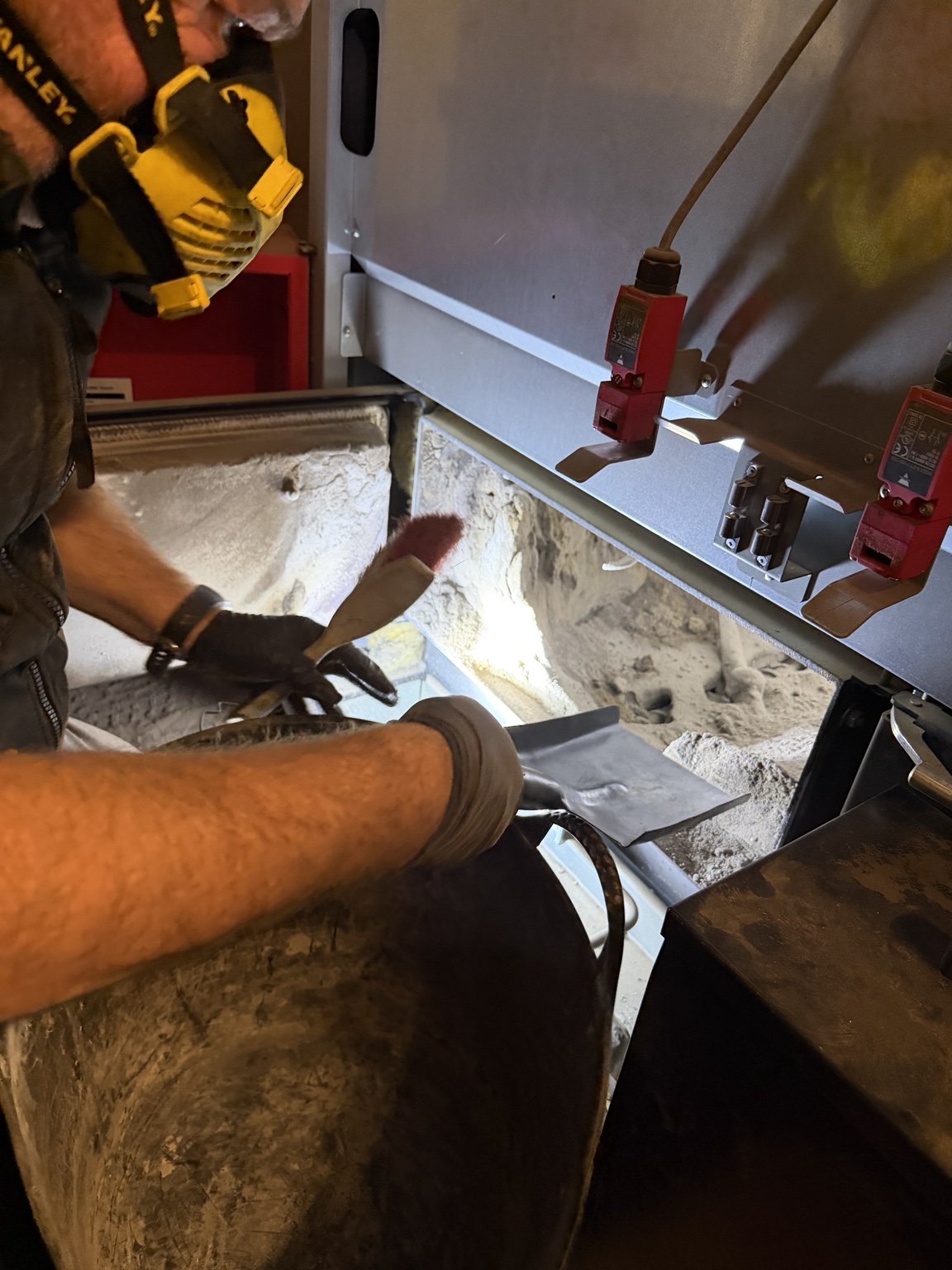 Engineer wearing a respirator brushing and collecting ash inside the Fröling biomass boiler