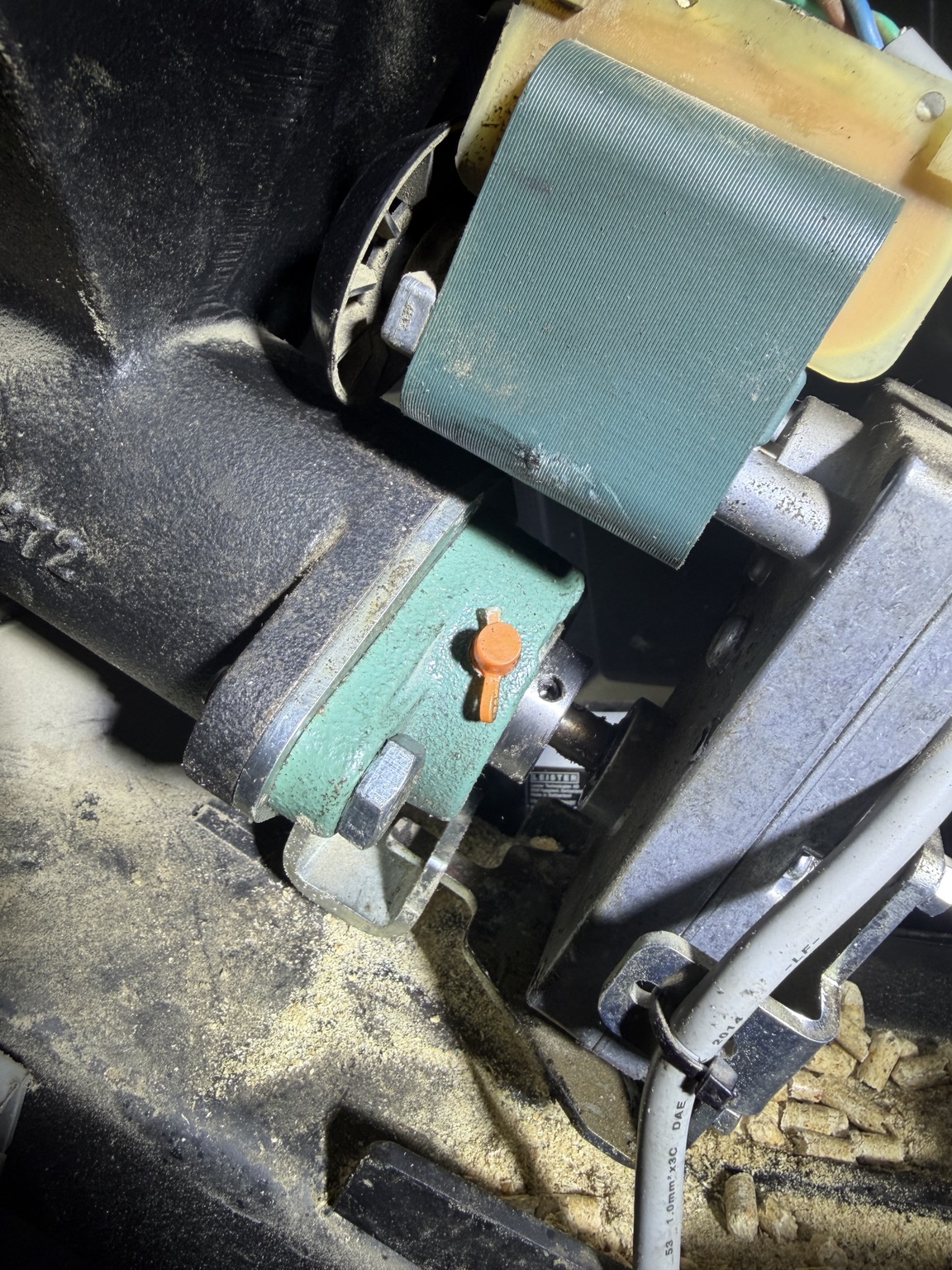 Close-up of a motor and mechanical assembly beside wood pellets inside the biomass boiler